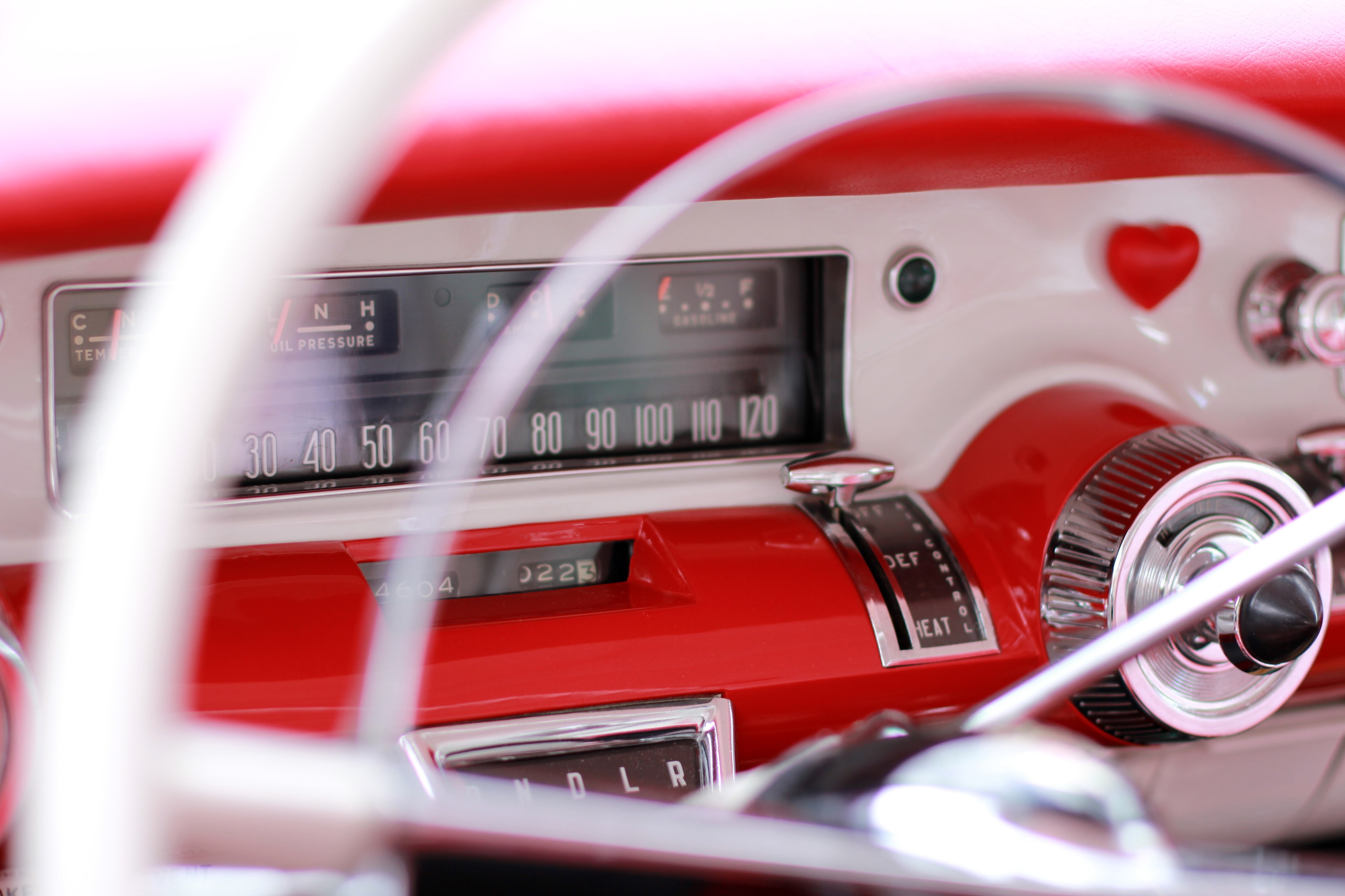 Picture of a restored classic car interior zoomed in on the red and white dashboard and steering wheel.